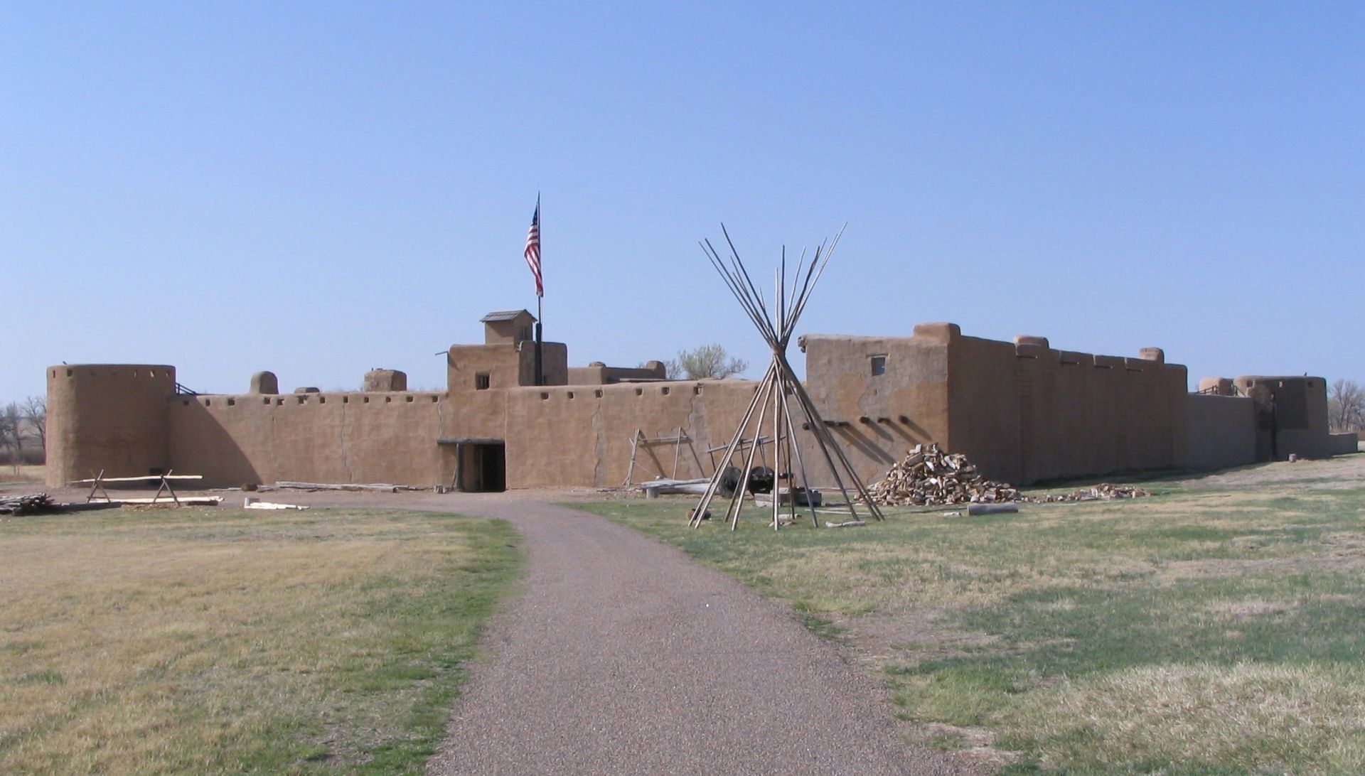Reconstructed adobe walls of Bent's Old Fort on the Arkansas River, with the central courtyard and bastion visible under a cloud-streaked Colorado sky.