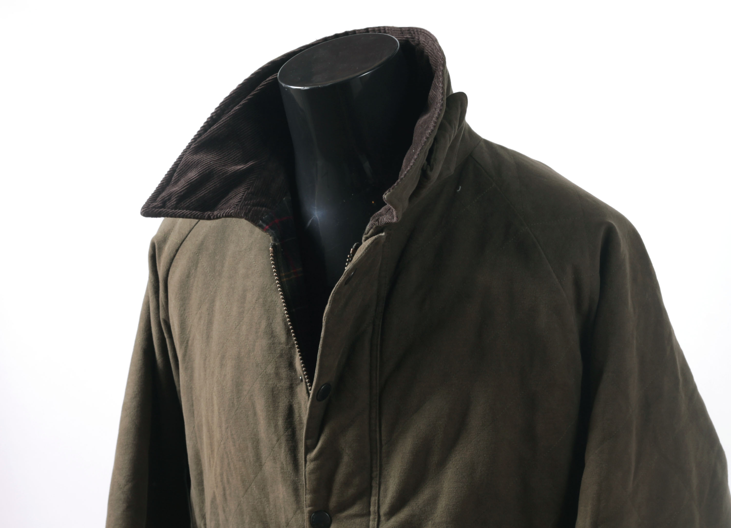 An olive-green waxed cotton Barbour jacket on a mannequin, showing the matte, slightly waxy surface of waxed canvas fabric, with a corduroy collar and tartan lining visible at the open front.