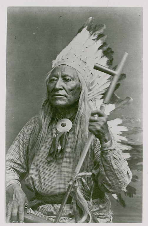 Period photograph of Chief Washakie in traditional regalia with Plains-style headdress, long braids, and a beaded shirt, looking directly at the camera.