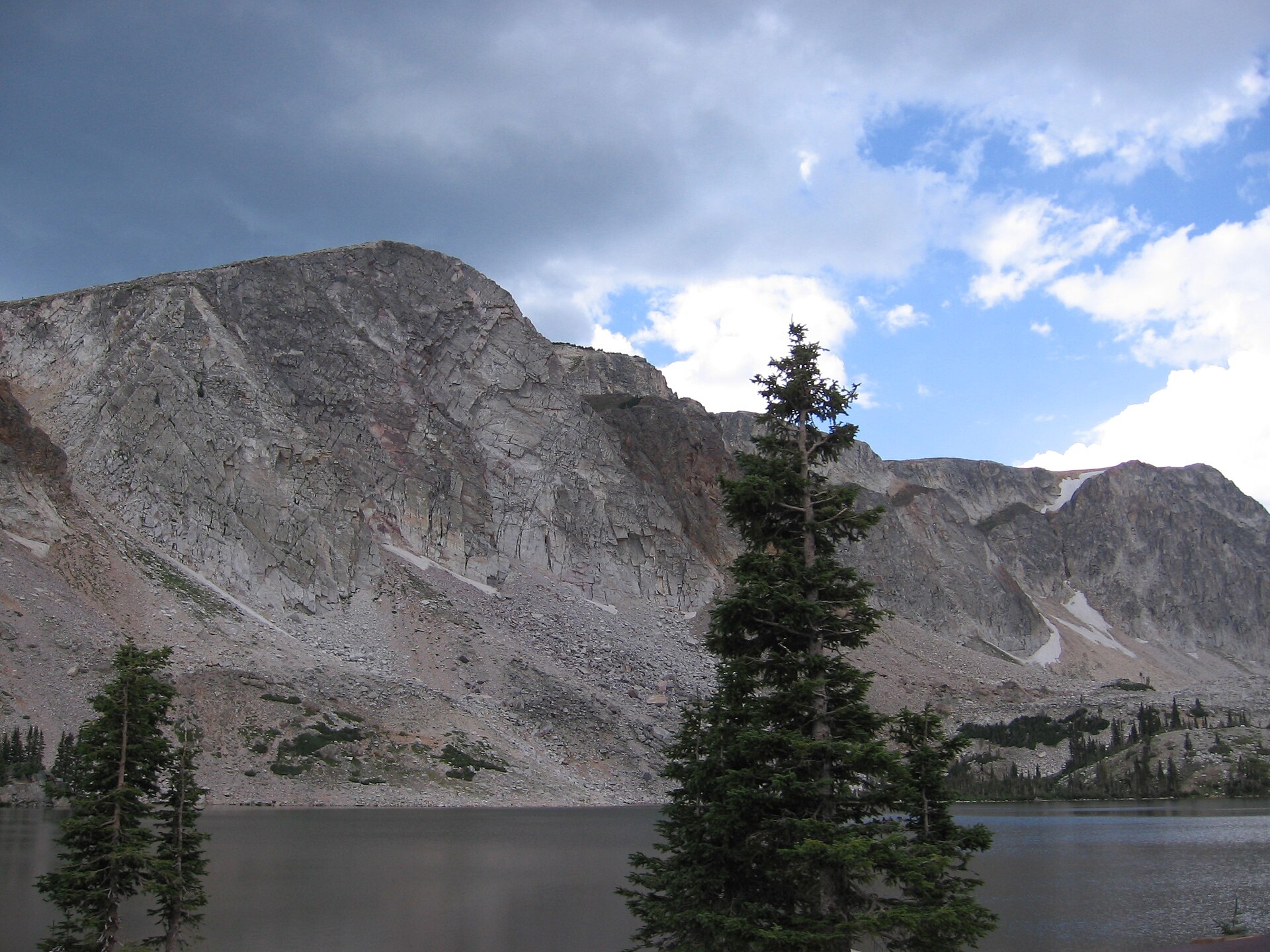 Mirror Lake reflecting Medicine Bow Peak in the Snowy Range, Wyoming, with summer wildflowers in the foreground and granite outcrops at the lake edge.