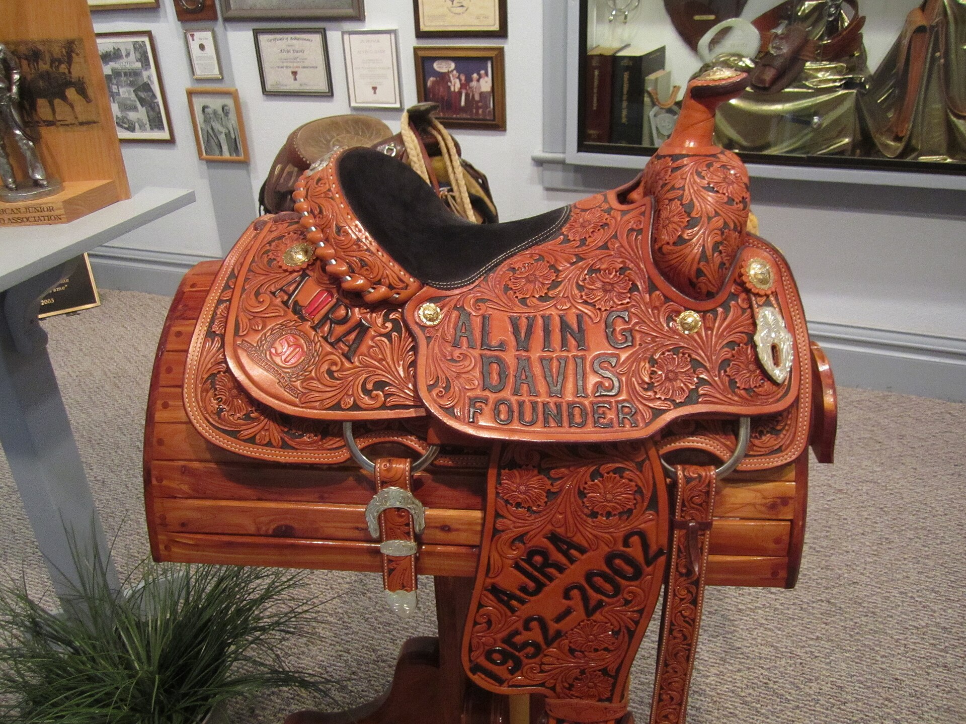 A hand-tooled Western saddle with a deeply carved floral and scrollwork pattern on the fender and skirt, resting on a rail.