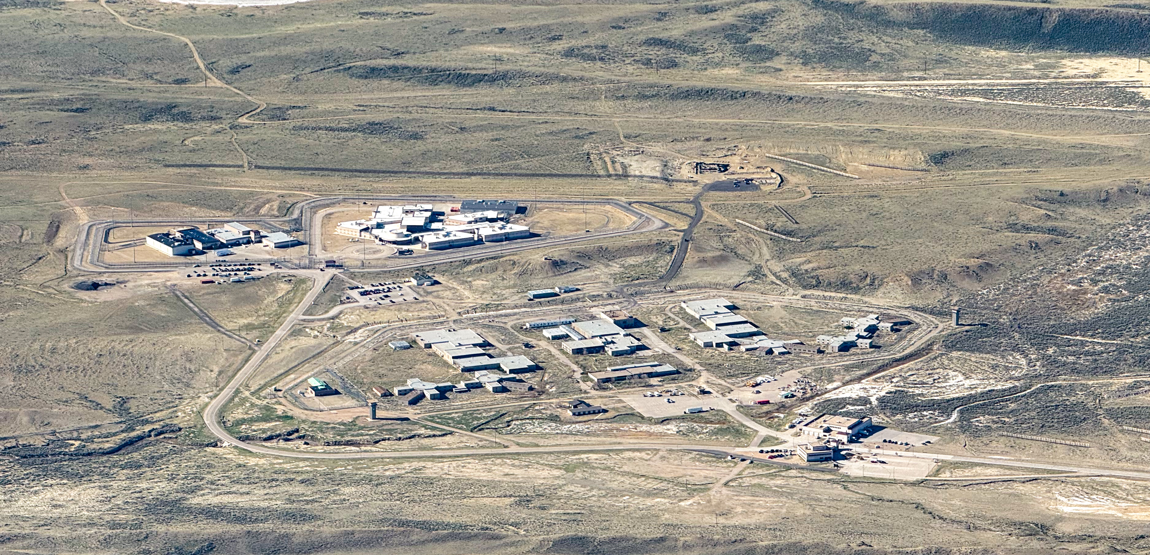 Aerial view of the Wyoming State Penitentiary in Rawlins, showing the full complex of cell blocks, guard towers, and prison yard against the high-plains landscape of Carbon County.