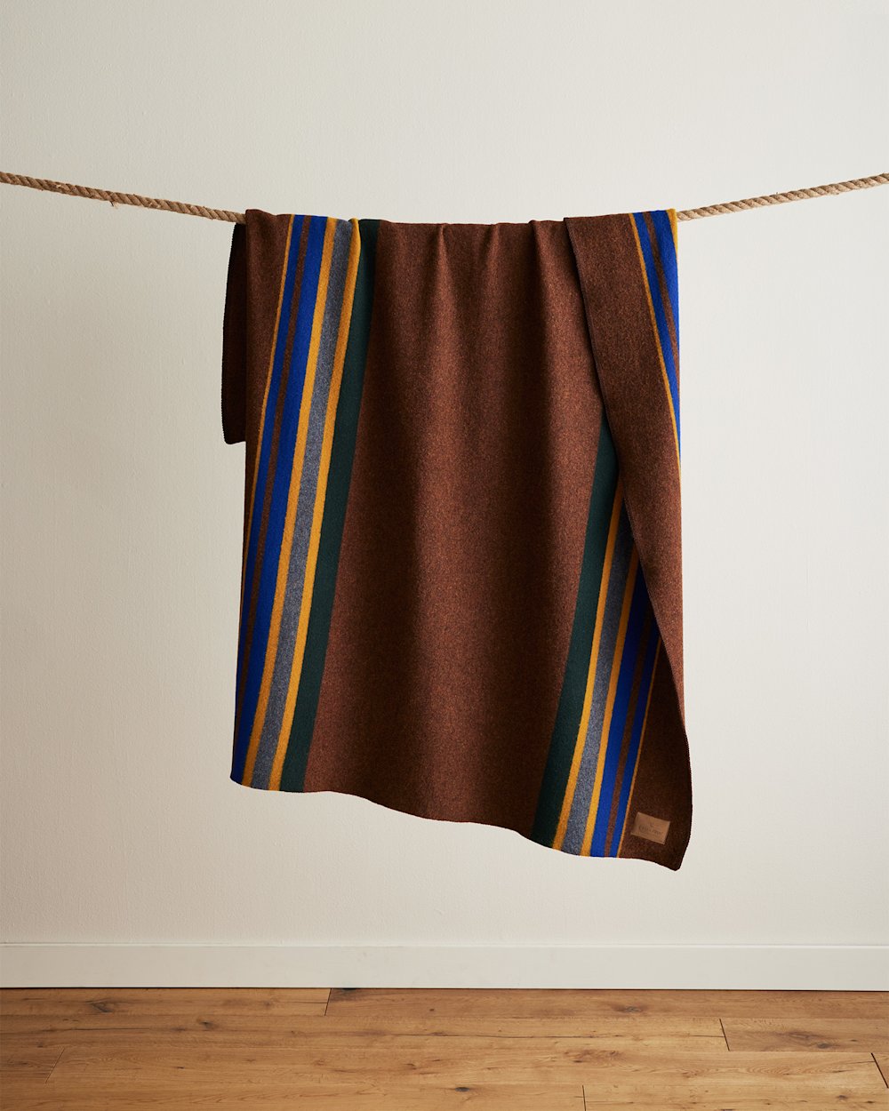 Pendleton Yakima Camp Throw in Umber colorway: rich brown field with vertical stripes in royal blue, gold, forest green, and gray, draped over a rope, 54 x 66 inches