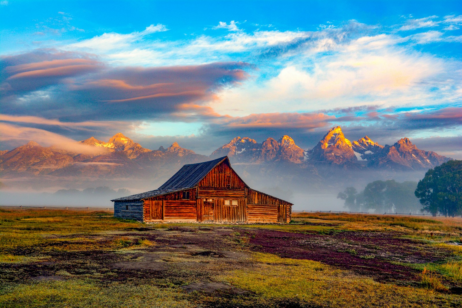 Weathered brown barn on open grassland with the Teton range rising directly behind.